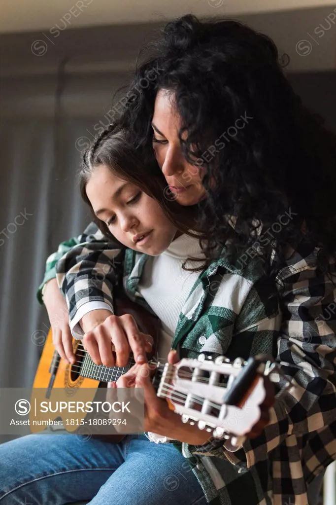 Mother teaching little daughter how to play acoustic guitar