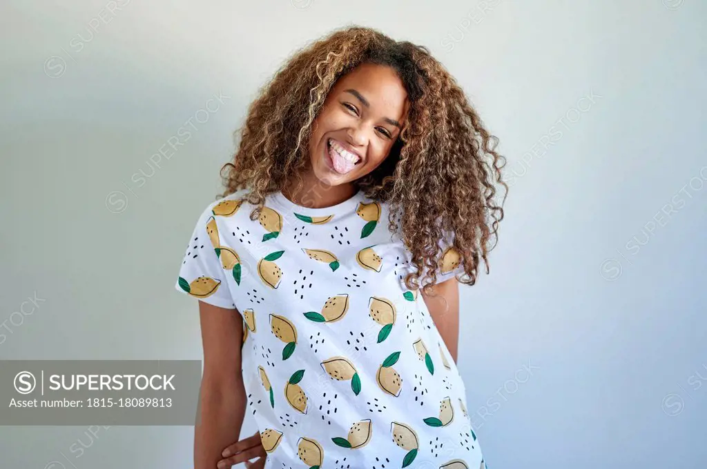 Afro happy woman sticking out tongue against white wall