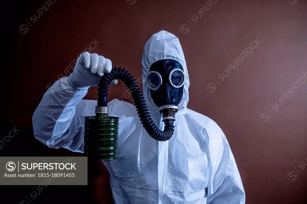 Mature in protective coveralls holding pipe of gas mask