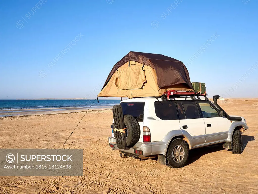 Tent pitched on top of roof of off-road vehicle parked on sandy coastal beach