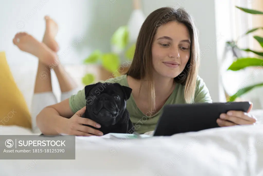 Young woman embracing Pug dog while using digital tablet at home