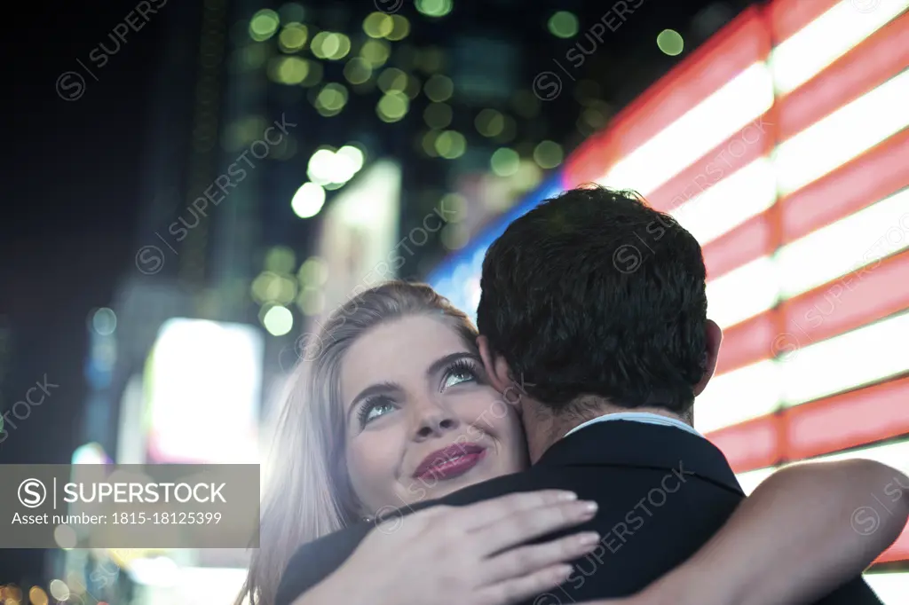 Beautiful woman embracing boyfriend by illuminated lights in city
