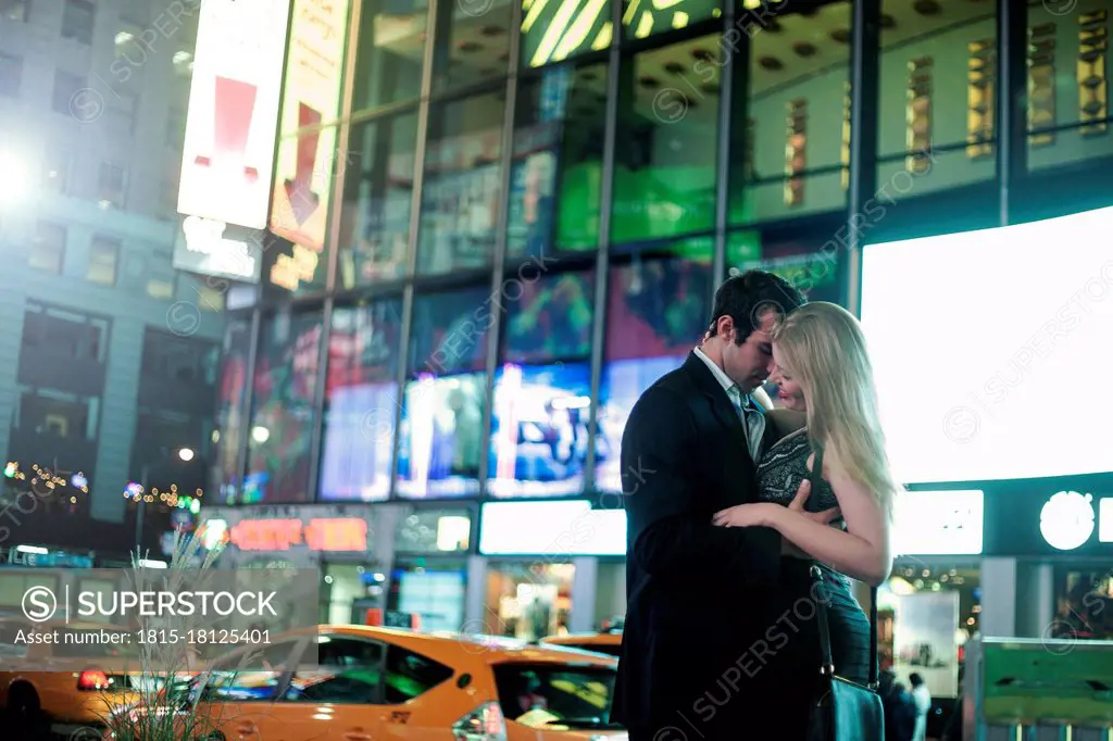 Happy young couple embracing on street in city during night
