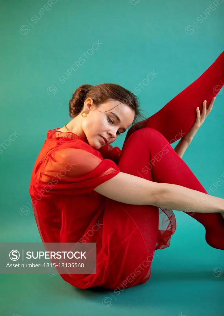 Beautiful woman doing ballet dance while sitting on turquoise floor