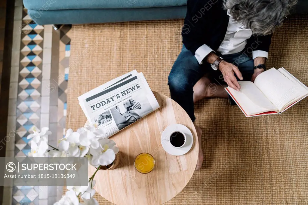 Man reading book while coffee and juice by newspaper on wooden table at home