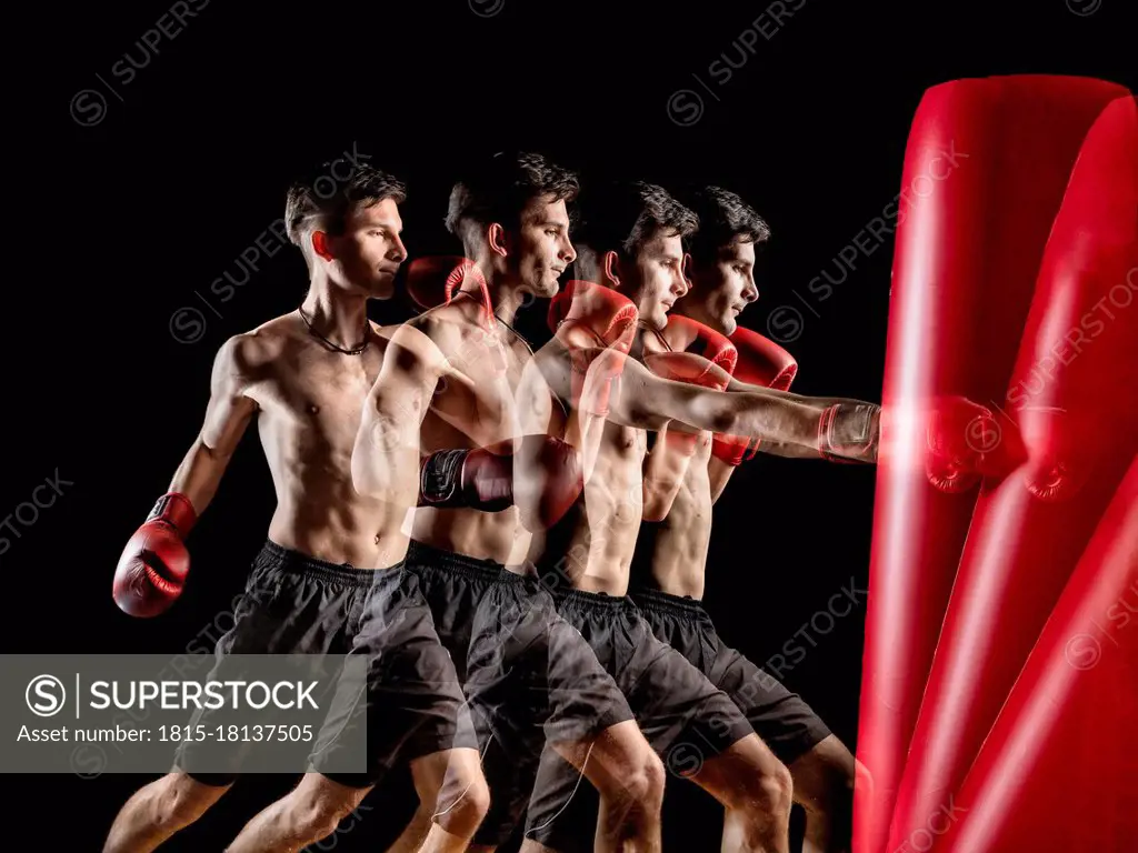 Young male boxer punching red bag against black background