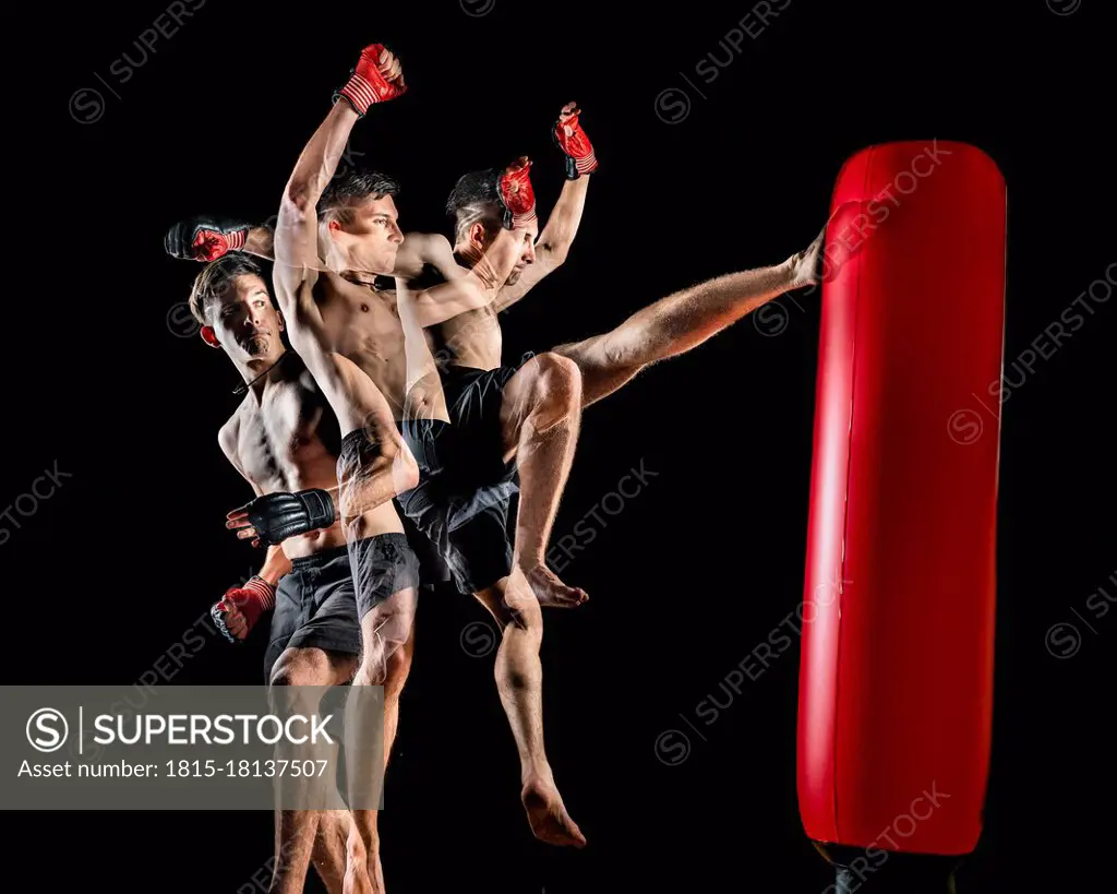 Young shirtless male martial arts athlete kicking punching bag over black background