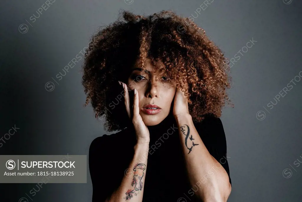 Curly haired woman with hand on face over grey background