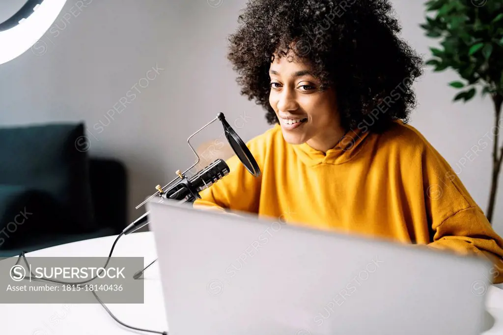 Young woman podcasting while looking at laptop at home