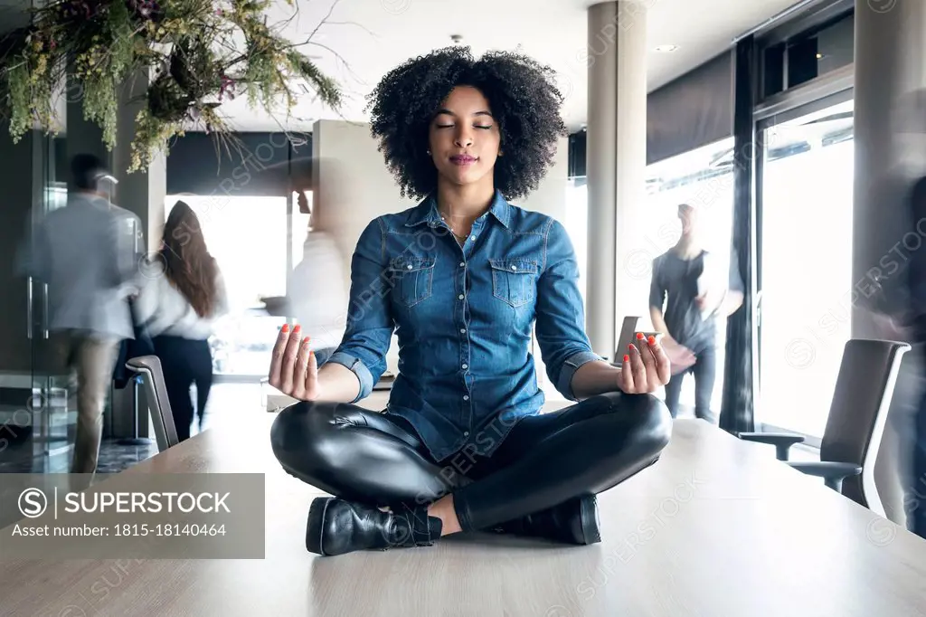 Young female professional meditating on conference table at office