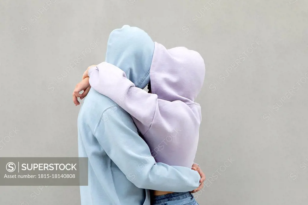 Couple in hooded shirt embracing each other by wall