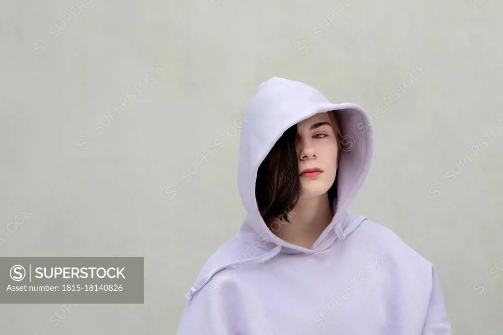 Beautiful teenage girl in hooded shirt by wall