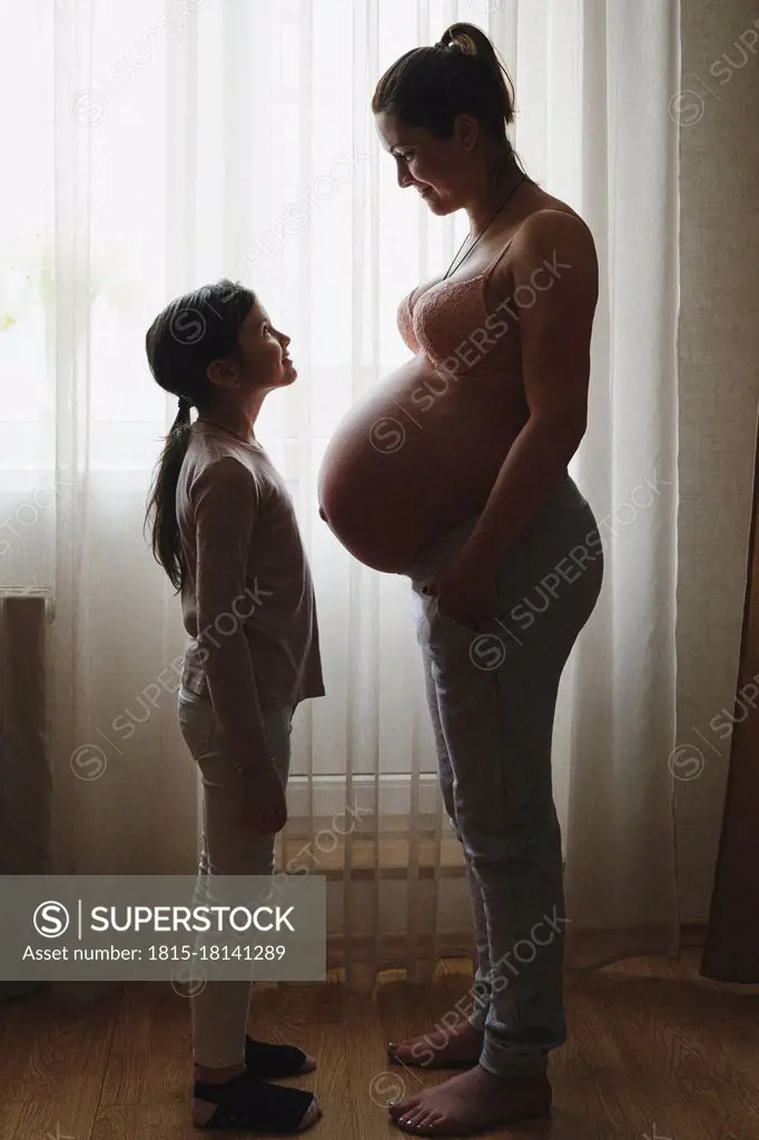 Pregnant mother standing with daughter at home