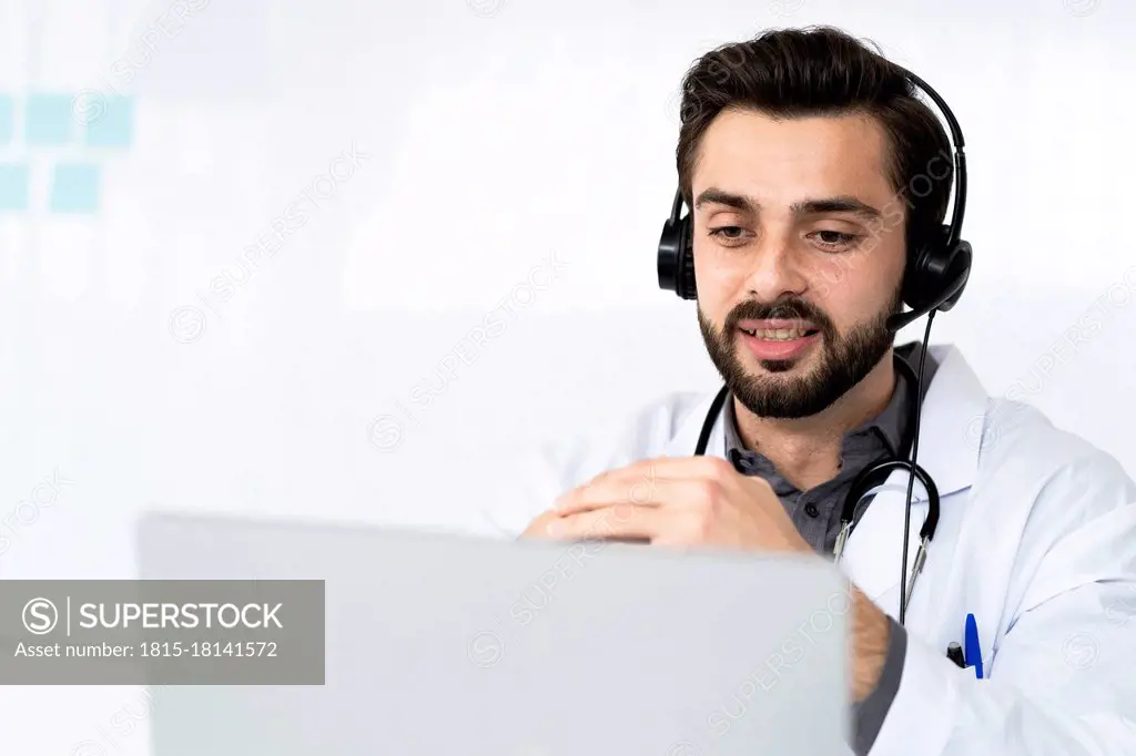 Male doctor wearing headphone while discussing on video conference at hospital