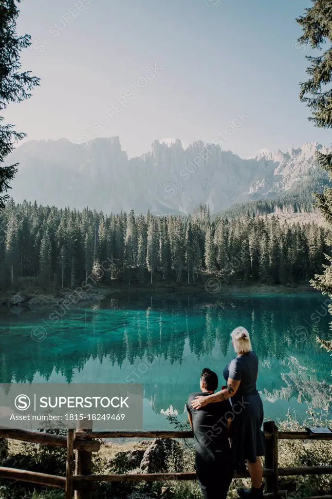 Couple looking at view while standing near railing at Carezza lake in South Tyrol, Italy