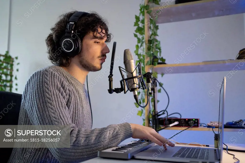 Male music composer with sound recording equipment using laptop at home