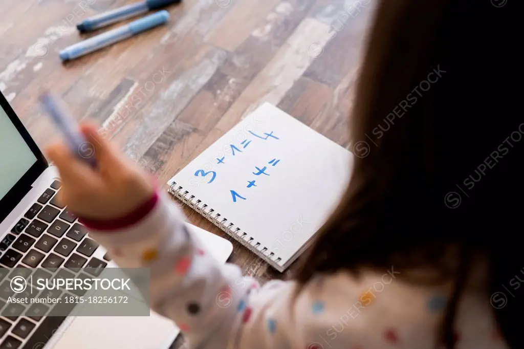 Girl with book and laptop studying Mathematics at home