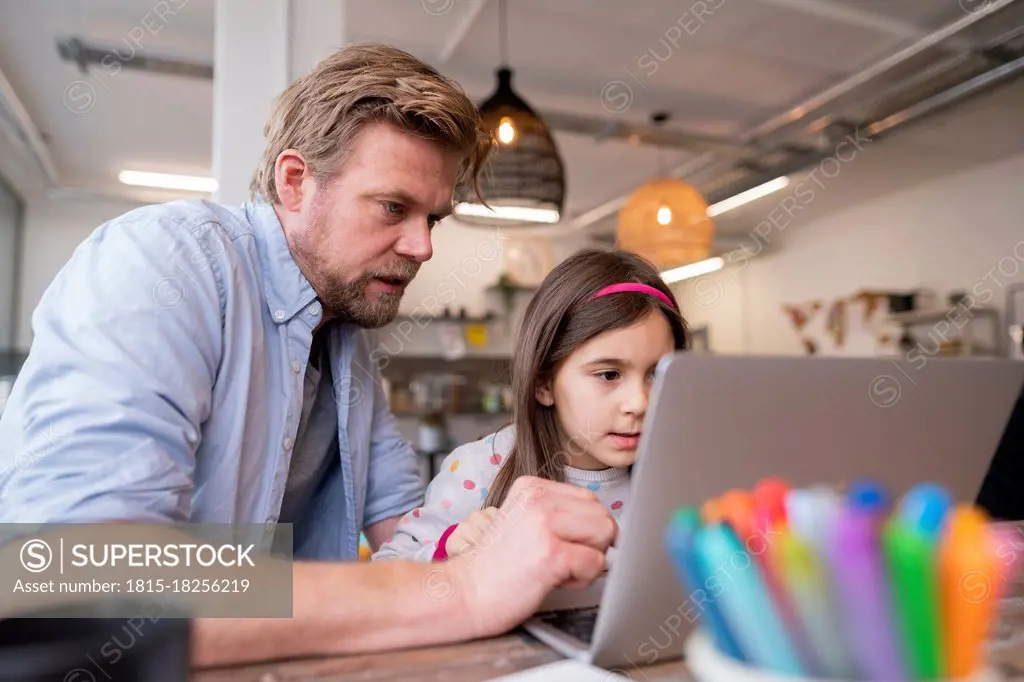 Mature man assisting girl e-learning through laptop at home