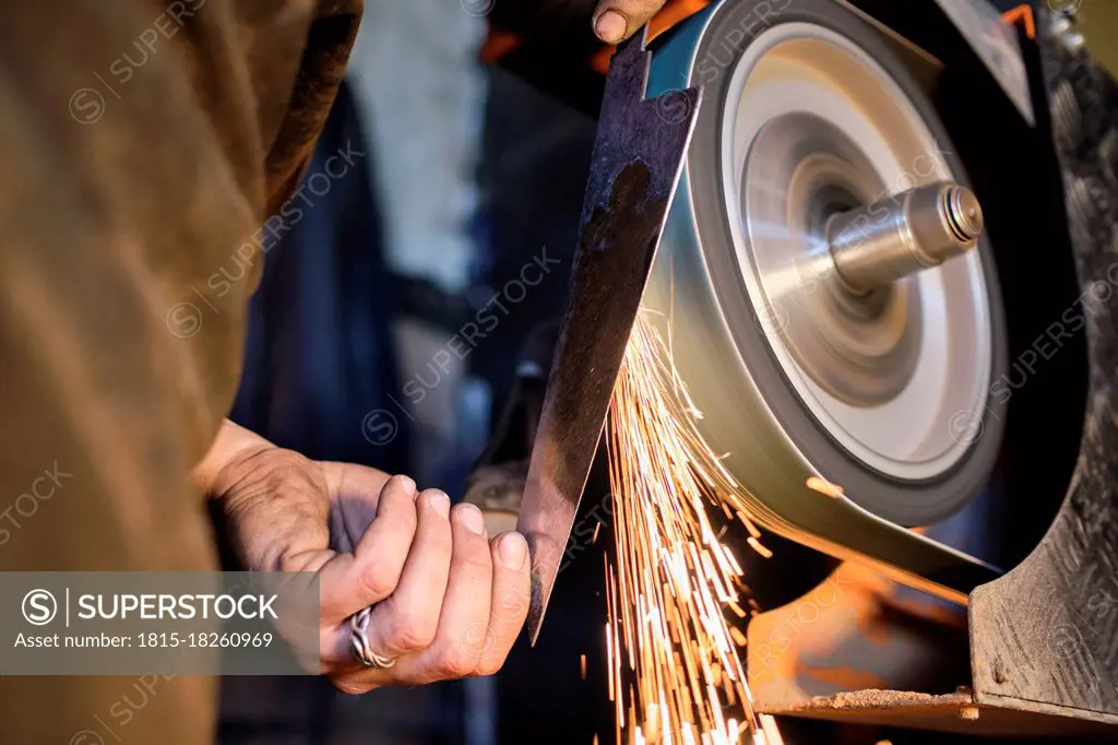 Male blacksmith sharpening knife shape metal on grinder at workshop