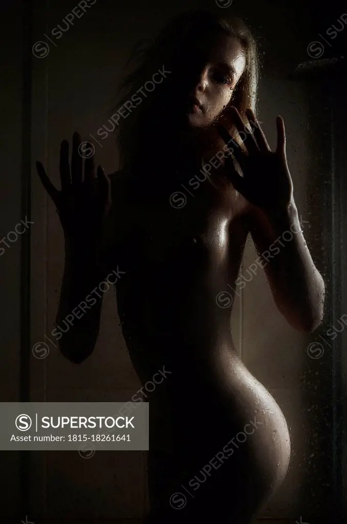 Naked young woman behind glass in bathroom