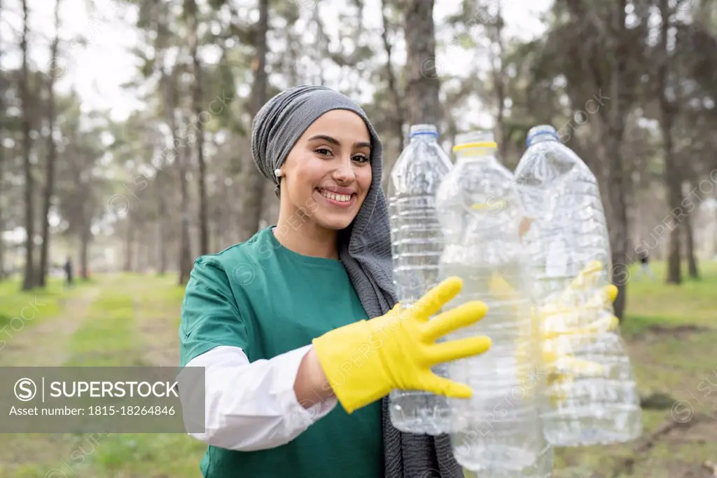 Smiling female volunteer with protective glove holding plastic bottle in forest