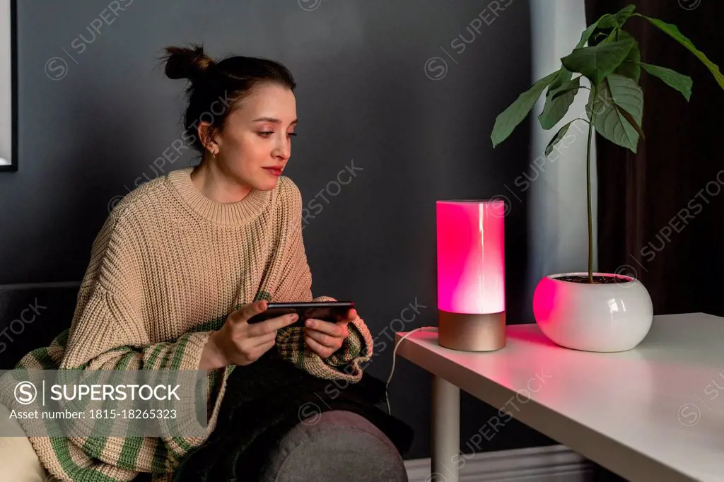 Woman looking at lighting equipment on table by plant at home