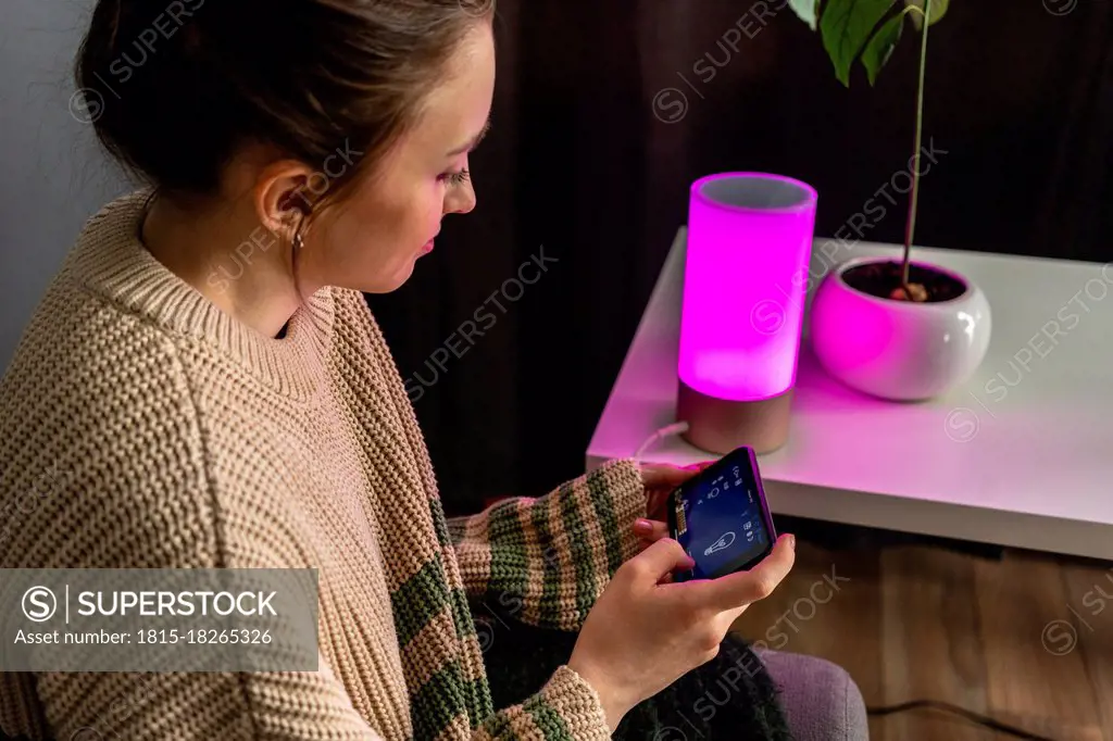 Young woman operating lighting equipment through mobile phone at home