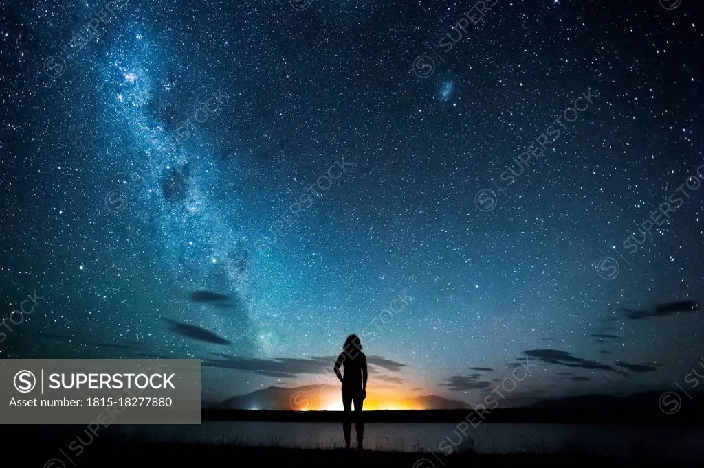 New Zealand, Canterbury, Twizel, Silhouette of man looking at Lake Poaka under starry sky