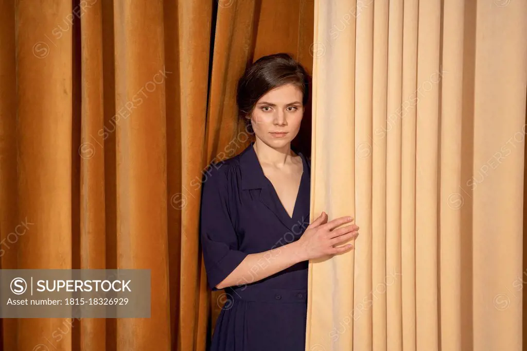 Confident young woman standing by curtain