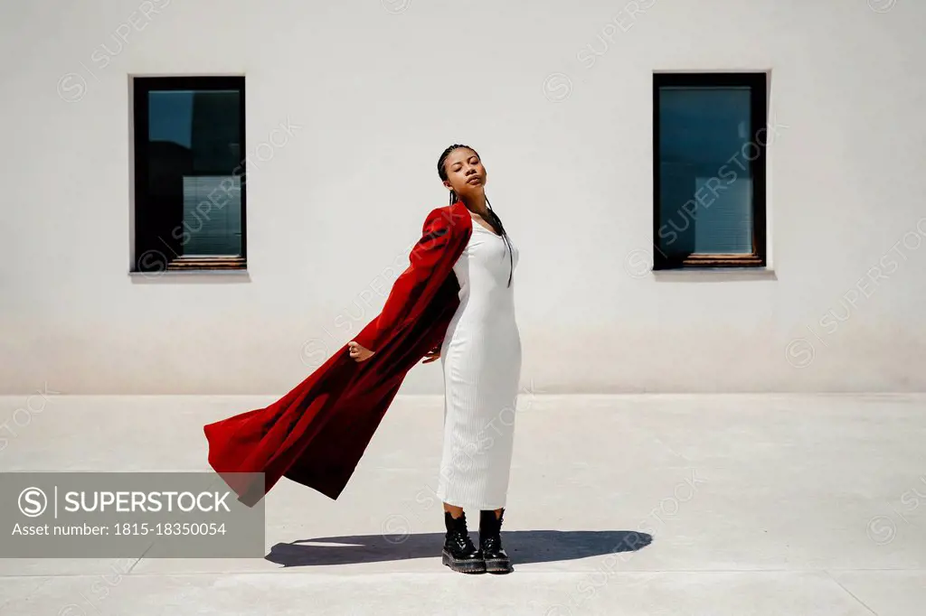 Serene woman blowing overcoat while standing on footpath