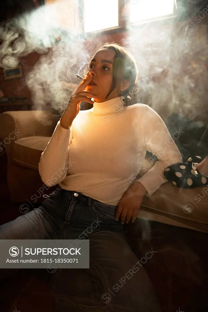 Thoughtful woman looking away while smoking cigarette at home