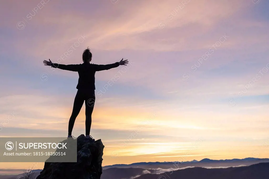 Young woman with arms outstretched standing on rock