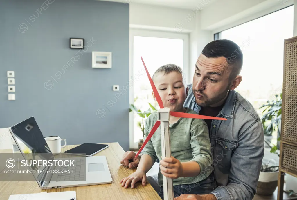 Male freelancer with son blowing wind turbine while playing at home