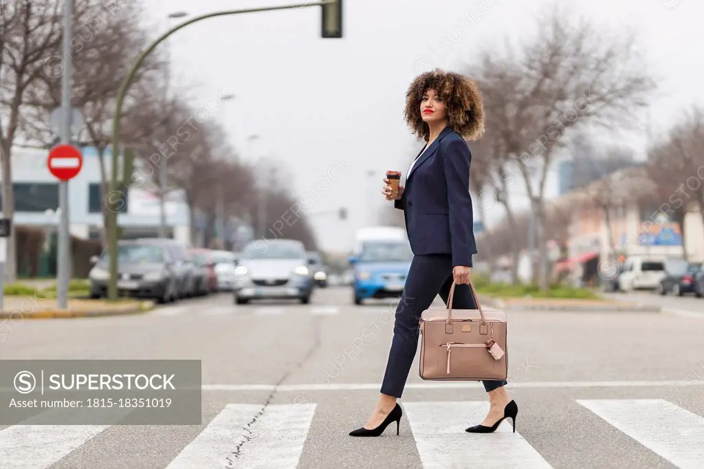 Well-dressed businesswoman with purse crossing road in city