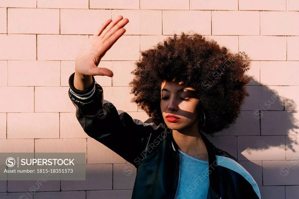 Afro hair young woman stretching hand in front of brick wall