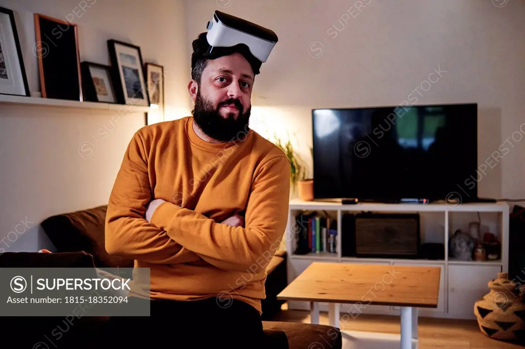 Mature man with arms crossed wearing virtual reality simulator at home