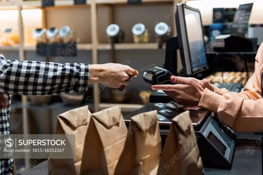 Female owner with card reader receiving payment from customer at supermarket