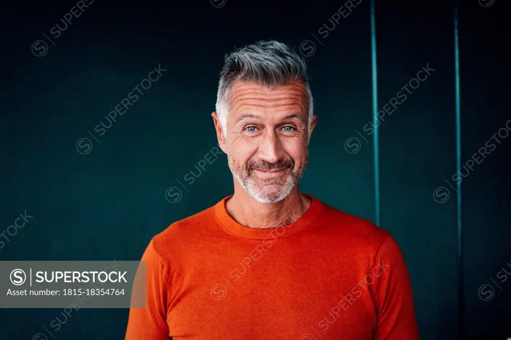 Mature man smiling in front of green wall
