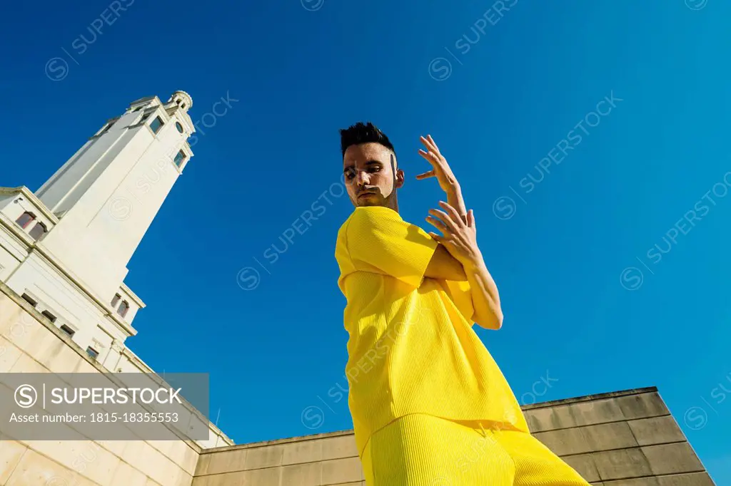 Young man gesturing while dancing by building during sunny day