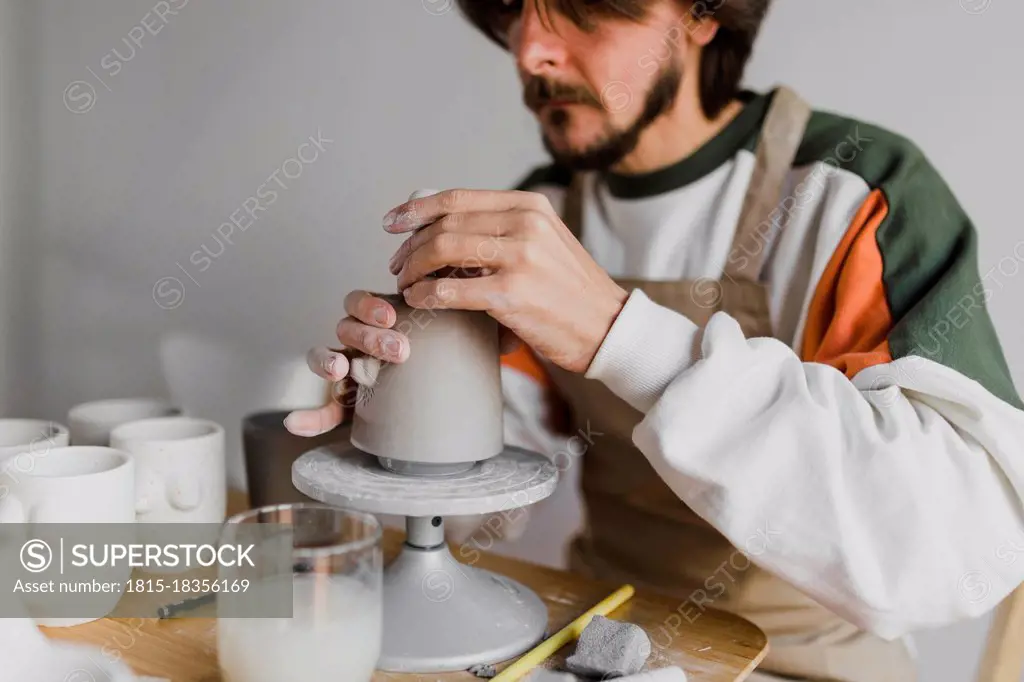 Male expert molding clay on pottery wheel at workplace