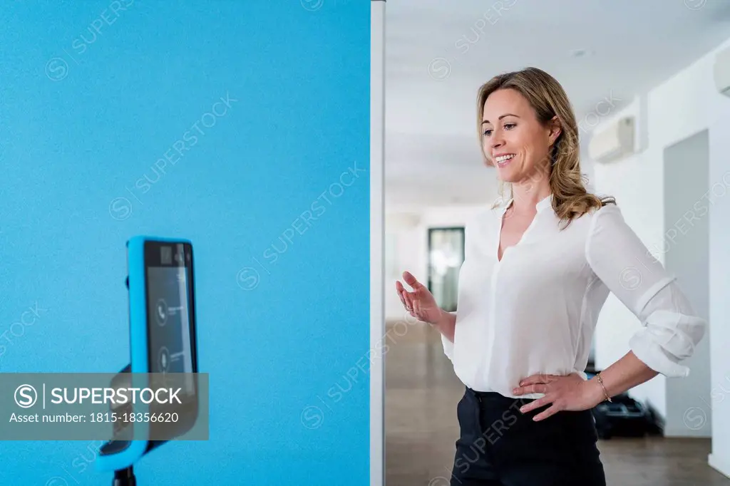 Businesswoman with hand on hip gesturing in front of assistant robot at office