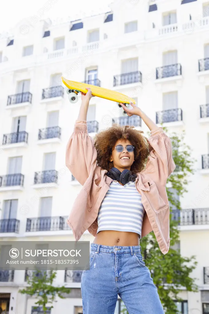 Cheerful young woman looking away while holding yellow skateboard