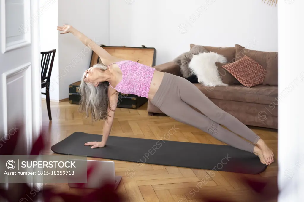 Mature woman wearing sports clothing practicing yoga at home