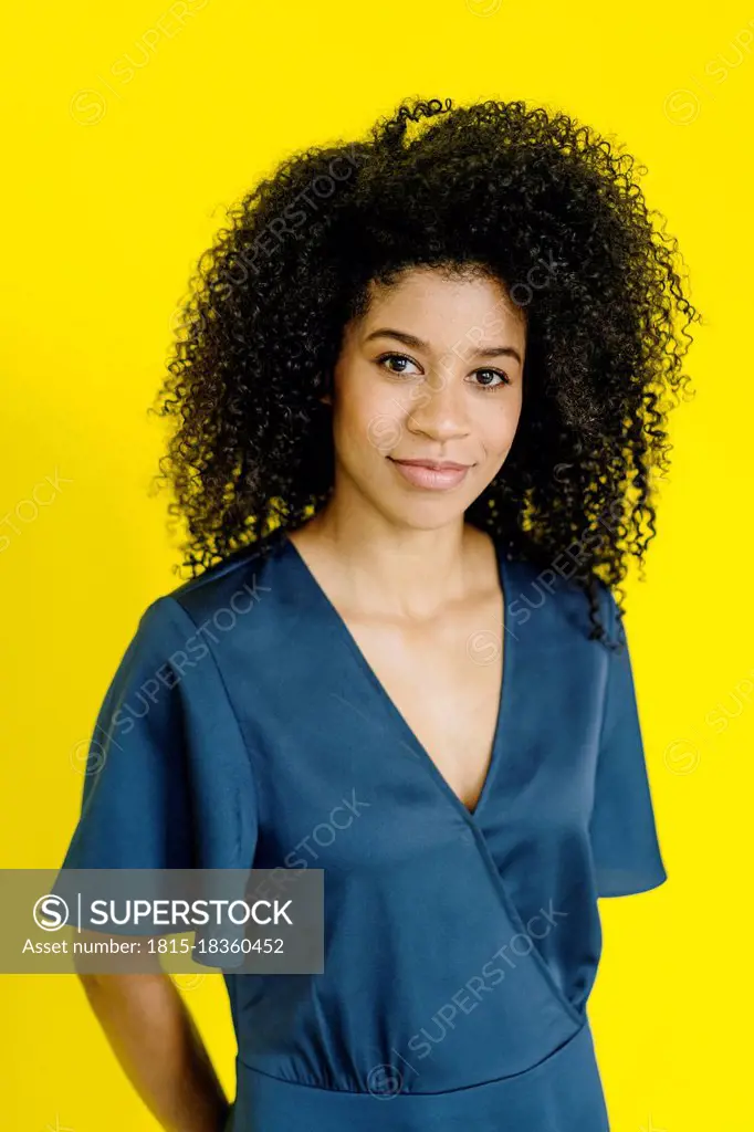 Businesswoman with frizzy hair standing at yellow background