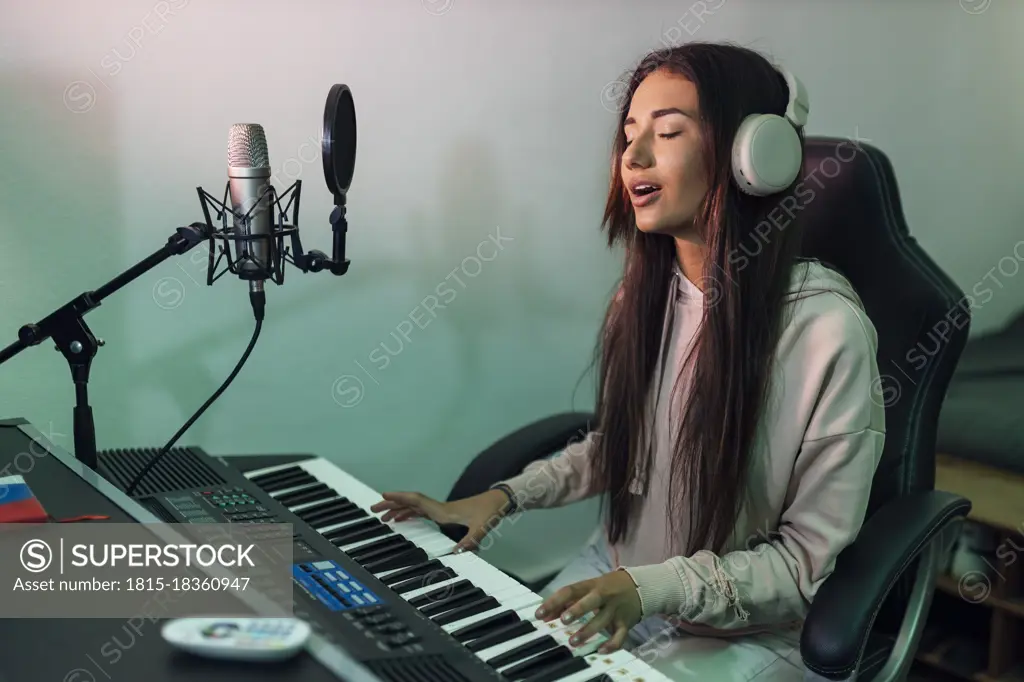 Young female singer singing while playing piano in studio
