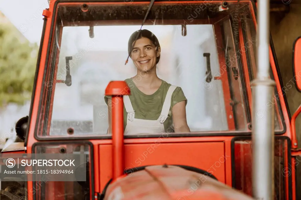 Smiling female farm worker sitting in tractor seen through windshield