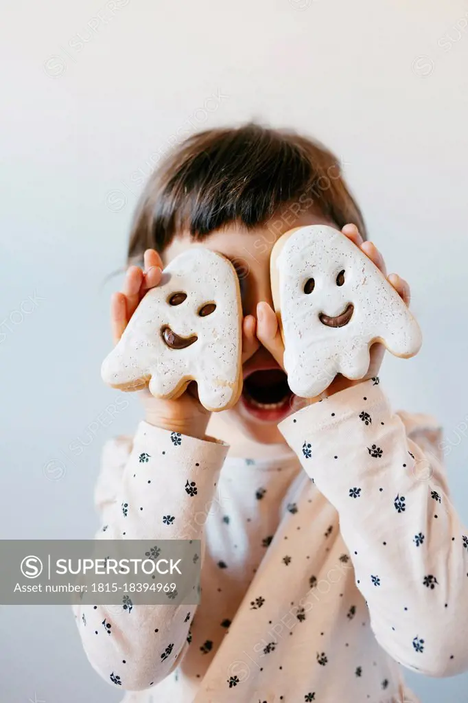 Little girl with mouth open covering eyes with ghost cookies
