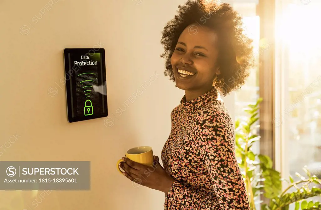 Cheerful woman with coffee cup standing by home automation device