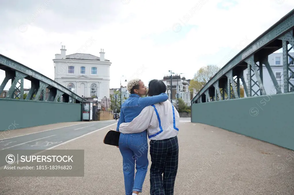 Lesbian woman with arm around kissing girlfriend walking on bridge