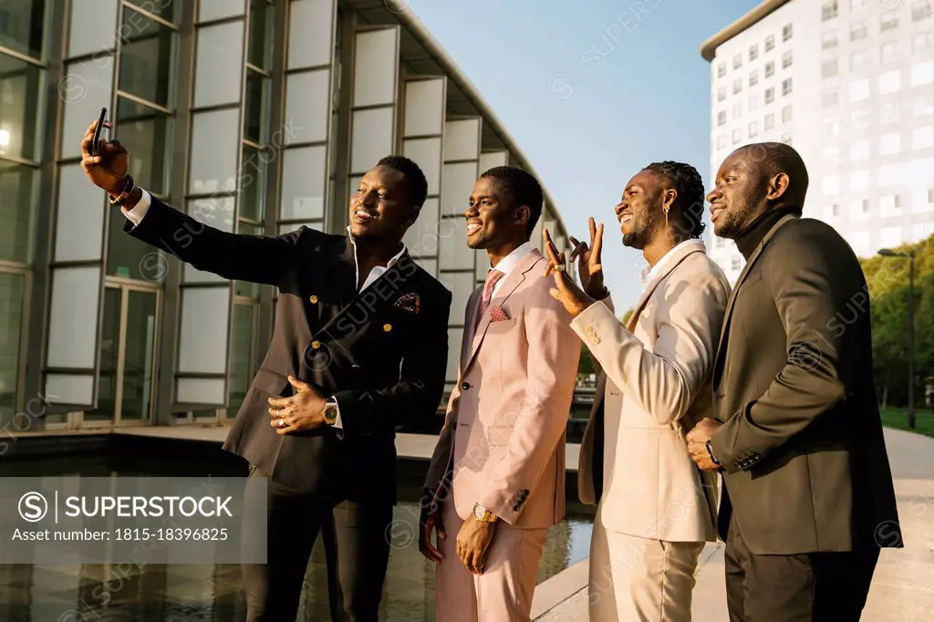 Male friends taking selfie through smart phone in city